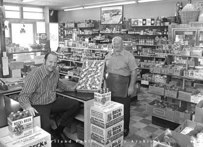 Interior of Model Foods Market, with proprietors Saul Goldberg (left) and Myer Goldberg (right) in his signature leather apron, in 1972.